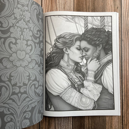 A coloring book (titled "The Sapphic Pirate Coloring Book: 30 Grayscale and Line Art Coloring Pages" by N.C. Starshadow) opened to display a black-line image of two sapphic pirates kissing.