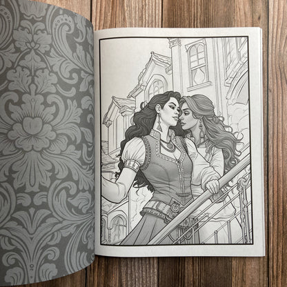 A coloring book (titled "The Sapphic Pirate Coloring Book: 30 Grayscale and Line Art Coloring Pages" by N.C. Starshadow) opened to display a black-line image of two sapphic pirates embracing.