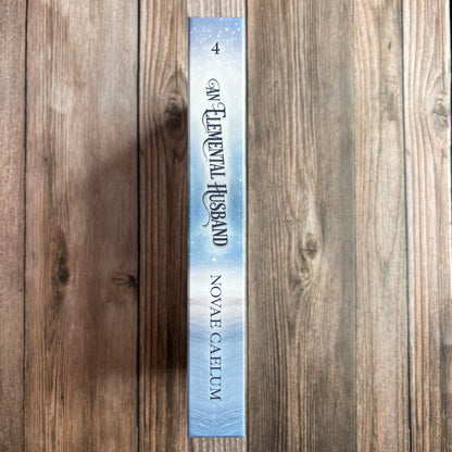 Spine of the hardcover "An Elemental Husband: The King's Weaver Book 4" by Novae Caelum, lying on a wood background, showing the "4" volume number and icy blue cover design.
