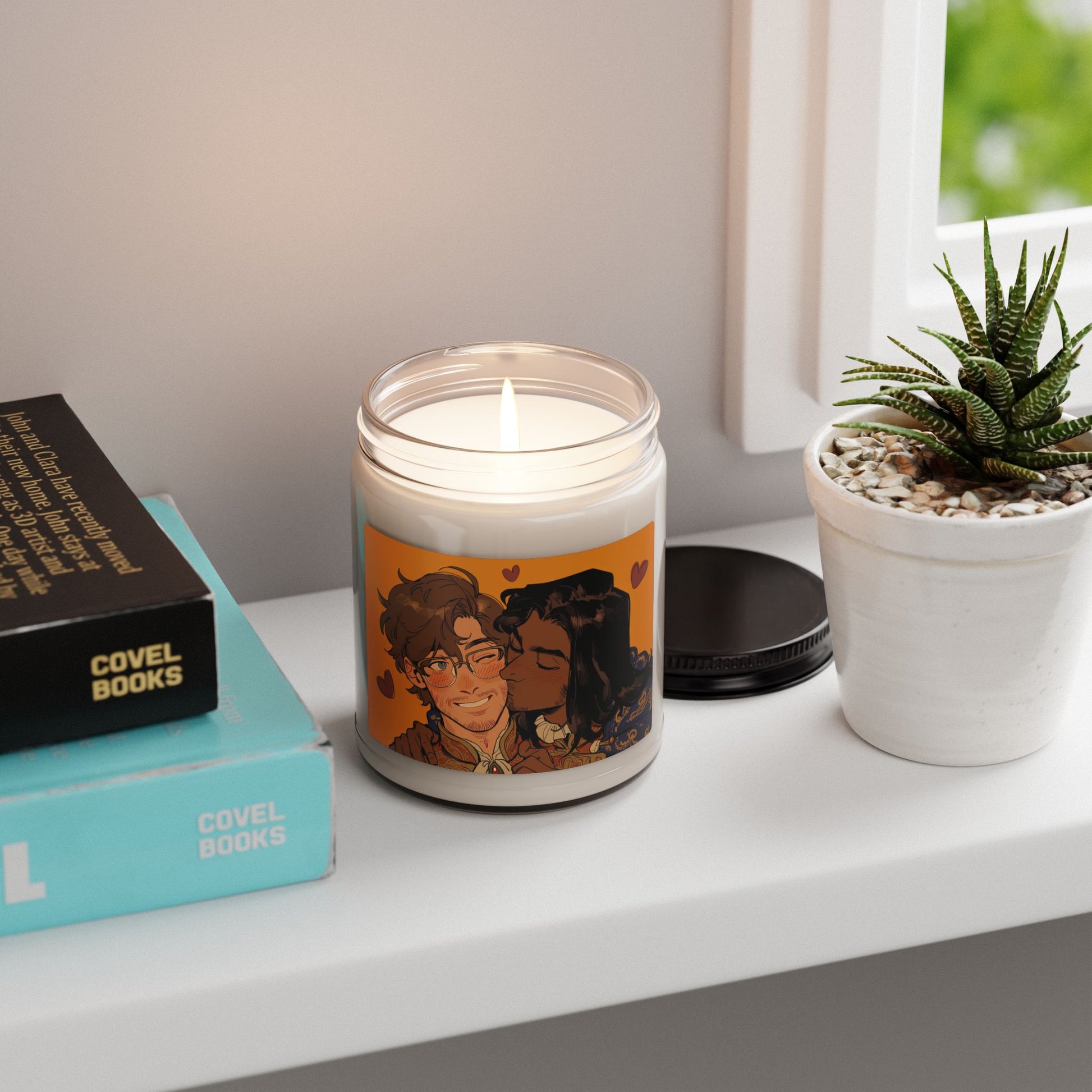 Lit 9oz soy candle on a windowsill beside books and a small succulent, label art of the smiling couple on an orange background with hearts.