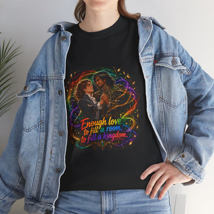 Black unisex t-shirt worn by a woman with long wavy brown hair, layered under an open denim jacket, printed with fantasy art of two men in formal attire dancing, wrapped in swirling rainbow magic and gold leaves, and the quote "Enough love to fill a room, to fill a kingdom."