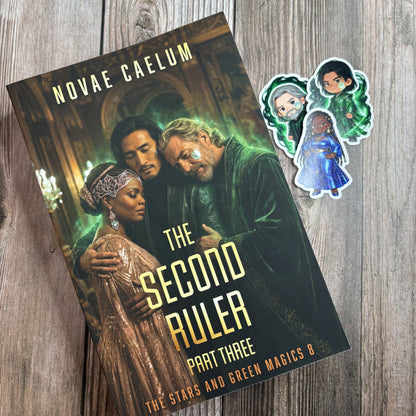 Character-art edition paperback of "The Second Ruler: Part Three" by Novae Caelum lying at an angle on weathered wood with three chibi character stickers beside it.