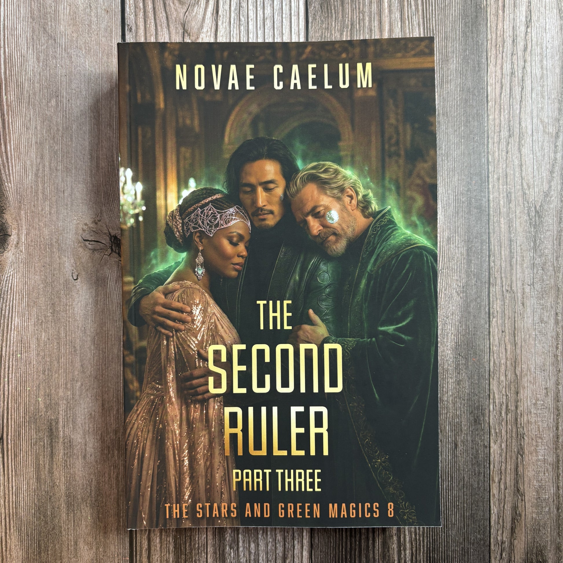 Front cover of the character-art edition of "The Second Ruler: Part Three — The Stars and Green Magics Book 8" by Novae Caelum, paperback on weathered wood showing three people embracing in a gilded, green-lit hall: a Black woman in a beaded headpiece and rose-gold gown, a dark-haired man of East Asian descent, and a white-bearded man in green velvet robes.